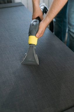 Temizlik şirketi çalışanı, profesyonel malzemelerle mobilyaların tozunu alıyor. Erkek kol temizleme koltuğu ve elektrikli süpürge.