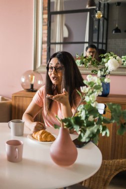 Happy couple eating breakfast and talking at dining table in morning. Indian girl and latin guy. Relationship and diversity