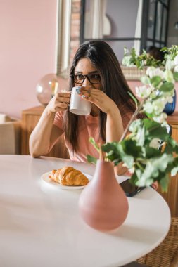 Portrait smart confident smiling millennial indian woman. Attractive young hindu teenager student girl freelancer during breakfast tea with croissant