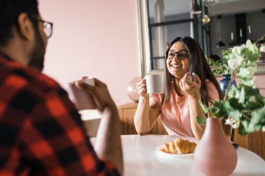 Young diverse loving couple eating croissant and talks together at home in breakfast time. Communication and relationship
