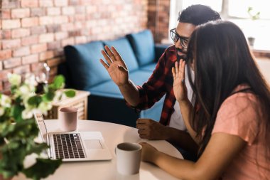 Latino or indian man and woman couple use their laptop in the living room to make video calls. Video call and online chat with familys