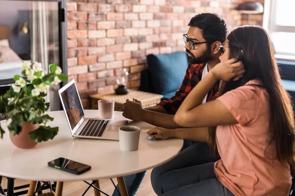 stock image Happy family couple cuddle at desk make video call to friends using laptop webcam. Loving young spouses look at computer screen waving hands in good mood greeting parents communicating online via app