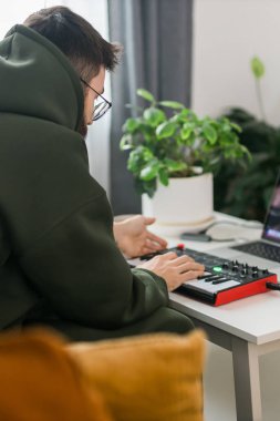 Recording electronic music track with portable midi keyboard on laptop computer in home studio. Producing and mixing music, beat making and arranging audio content with professional audio devices