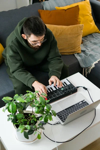Recording electronic music track with portable midi keyboard on laptop computer in home studio. Producing and mixing music, beat making and arranging audio content with professional audio devices