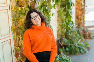 Portrait of carefree young woman smiling with urban background. Cheerful latin girl wearing eyeglasses in the city. Happy brunette woman with curly hair spectacles smiling.