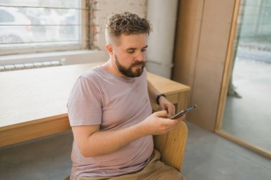 Portre hayal kırıklığına uğramış, kafası karışmış, üzgün, genç, yakışıklı adam kameraya bakıyor, akıllı telefondan olumsuz haberler alıyor.