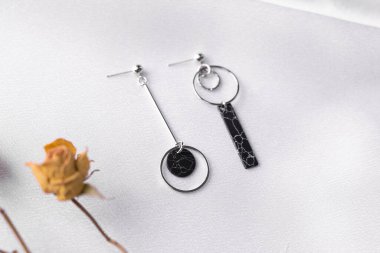 Kurumuş çiçeklerle birlikte ipek arka planda duran gümüş küpeli yaratıcı kompozisyon. Minimalist tarzda el yapımı aksesuarlar.