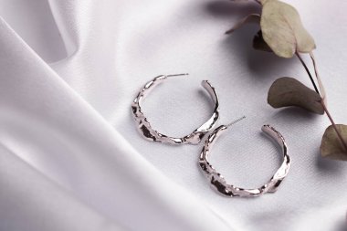 Kurumuş çiçeklerle birlikte ipek arka planda duran gümüş küpeli yaratıcı kompozisyon. Minimalist tarzda el yapımı aksesuarlar.