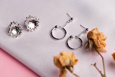Kurumuş çiçeklerle birlikte ipek arka planda duran gümüş küpeli yaratıcı kompozisyon. Minimalist tarzda el yapımı aksesuarlar.
