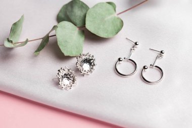 Kurumuş çiçeklerle birlikte ipek arka planda duran gümüş küpeli yaratıcı kompozisyon. Minimalist tarzda el yapımı aksesuarlar.