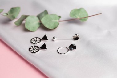 Kurumuş çiçeklerle birlikte ipek arka planda duran gümüş küpeli yaratıcı kompozisyon. Minimalist tarzda el yapımı aksesuarlar.