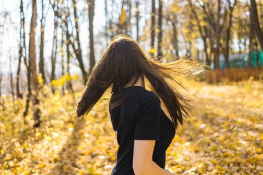Gün batımında parkta dans eden uzun tüylü, sevimli genç bir kadın. Gün batımında ormanda kahverengi saçlı güzel bir kadın dans ediyor. Özgürlük ve mevsim doğa kavramı. Yumuşak odak.
