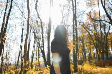 Gün batımında parkta dans eden uzun tüylü, sevimli genç bir kadın. Gün batımında ormanda kahverengi saçlı güzel bir kadın dans ediyor. Özgürlük ve mevsim doğa kavramı. Yumuşak odak.