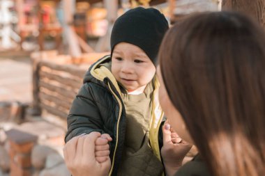 Anne ve küçük oğlu sonbahar parkında. Kadın çocuk ceketinin fermuarını çeker.