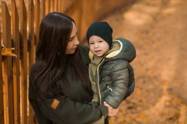 Sevimli küçük çocuk annesiyle dışarıda duruyor. Sonbahar parkında yürüyen mutlu çocuk. Küçük çocuk modaya uygun ceket ve şapka giyiyor. Sonbahar modası. Şık bir çocuk.