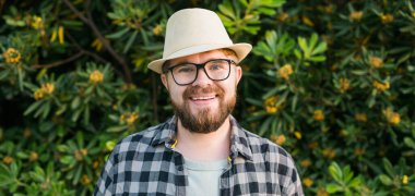 Laughing attractive man wearing hat over green tree background - emotion and vacation travel holidays