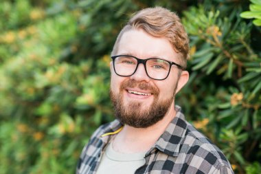 Laughing attractive man wearing hat over green tree background - emotion and vacation travel holidays