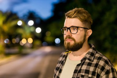 Portrait of man standing in night city street with bokeh street lights background. Confident lonely guy. Close-up portrait