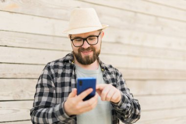 Gülümseyen erkek turist, yaz kenti boyunca ahşap duvarları aşarken akıllı telefon kullanıyor. Teknolojiler ve sosyal medya uygulaması.