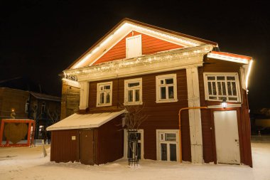 Geceleri parlayan Noel çelenkleriyle süslenmiş ahşap bir ev. Şehirde şenlik süslemeleri, çelenkler ve ışıklar.