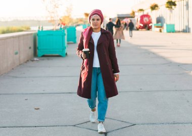 Caddede yürüyen tesettürlü, akıllı telefon dinleyen ve kahve içen genç, güzel bir Arap kadın. Başörtülü güzel bir kadın havaalanında geziniyor, mesaj atıyor ve içkisini yudumluyor..