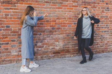 Kız, kız arkadaşının fotoğrafını tuğla duvarın önünde çekiyor.