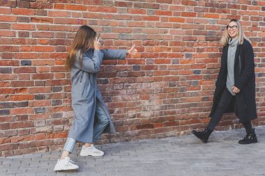 Kız, kız arkadaşının fotoğrafını tuğla duvarın önünde çekiyor.