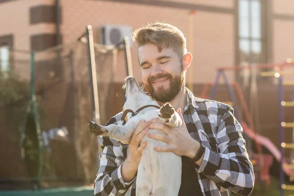 Happy young man holding dog jack russell terrier in hands at sunset outdoors. Pet owner