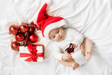 Noel Baba şapkalı çocuk hediye kutusuyla yatakta yatıyor ve ziyafet takıları takıyor..