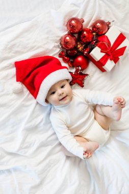 Noel Baba şapkalı çocuk hediye kutusu ve şenlikli mücevherlerle yatakta oturuyor..