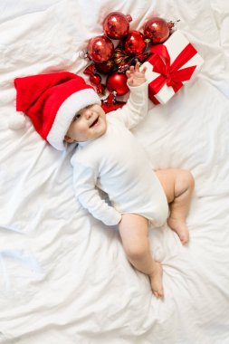 Noel Baba şapkalı çocuk hediye kutusuyla yatakta yatıyor ve ziyafet takıları takıyor..