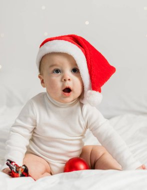 Noel Baba şapkalı çocuk hediye kutusu ve şenlikli mücevherlerle yatakta oturuyor..