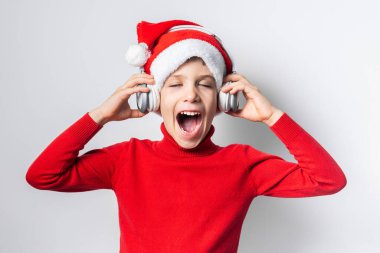 Çocuk elinde komik Noel Baba şapkasıyla Noel müziği dinliyor.