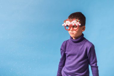 Noel Baba 'nın partisindeki şirin çocuk mavi arka planda Noel Baba gözlükleri. Başında kar olan çocuk fotokopi alanı ve maketi.