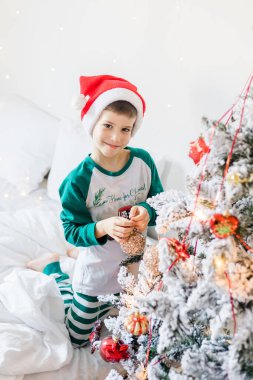 Çocuk Noel ağacını süslüyor. Çocuğun elinde bir Noel oyuncağı var. Noel 'den önceki sabah evde. Nesil alfa ve gen alfa çocukları
