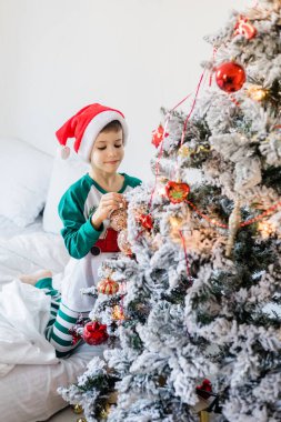 Çocuk Noel ağacını süslüyor. Çocuğun elinde bir Noel oyuncağı var. Noel 'den önceki sabah evde. Nesil alfa ve gen alfa çocukları