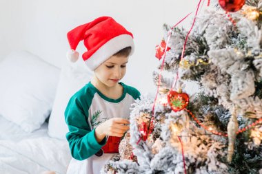 Çocuk Noel ağacını süslüyor. Çocuğun elinde bir Noel oyuncağı var. Noel 'den önceki sabah evde. Nesil alfa ve gen alfa çocukları
