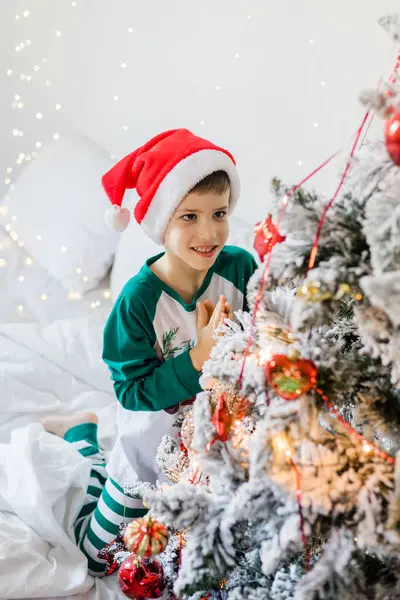 Child decorates Christmas tree. The boy is holding a Christmas toy. Morning before christmas at home. Generation alpha and gen alpha children