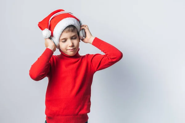 Funny child boy holds listening to Christmas music with Santa Claus hat on white background. Generation alpha and gen alpha children