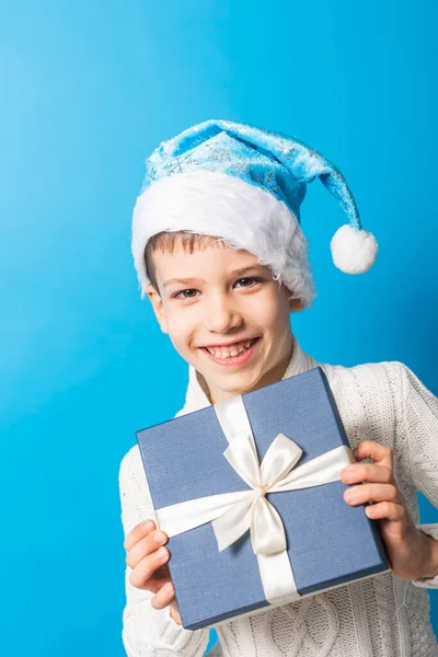 Hediye kutusu fotokopi alanı olan mavi Noel şapkalı küçük mutlu çocuk. Mesajın için boş yer. Kış tatili ve şimdiki konsept