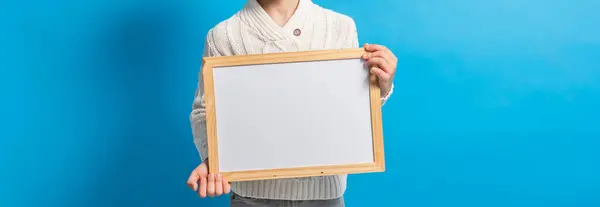 Banner boy with blank canvas. Copy space on canvas board for image or message. Kid holds mockup poster and standing over blue background