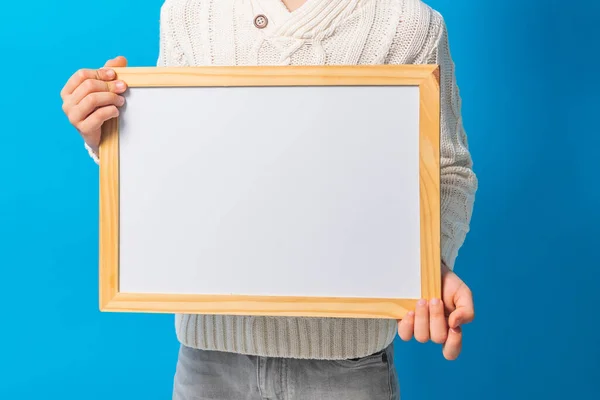 Close-up boy with blank canvas. Copy space on canvas board for image or message. Kid holds mockup poster and standing over blue background