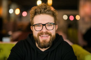 Kafede şık gözlükler takan genç ve serbest çalışan bir adamın yakın portresi. Kameraya, eğitime ve online çalışma konseptine bakan kendine güvenen mutlu öğrenci. Y jenerasyonu ve Y jenerasyonu