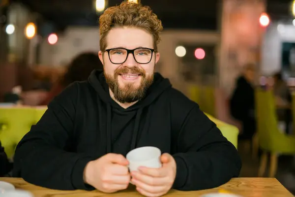 Bearded curly man smiling confident drinking coffee in restaurant or coffee shop. Millennial generation and Gen Y.