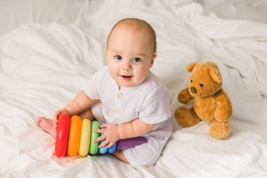 Beyaz yatak odasındaki bebek. Yeni doğmuş çocuk oyuncaklarla yatakta. Çocuklar için çocuk odası. Tekstil, yastık ve çocuklar için yatak. Aile sabahı evde. Oyuncak ayıyla yeni doğmuş çocuk zamanı