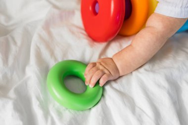 Beyaz güneşli yatak odasında renkli gökkuşağı oyuncak piramidiyle oynayan yakın plan bebek. Küçük çocuklar için oyuncaklar. Eğitici oyuncağı olan çocuk