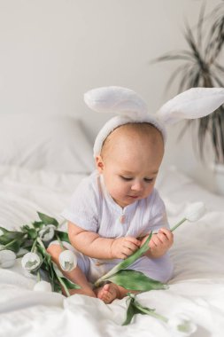 Kafasında tavşan kulakları ve yatağında laleleri olan sevimli bir bebek. Paskalya ve bahar zamanı