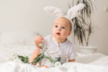 Kafasında tavşan kulakları ve yatağında laleleri olan sevimli bir bebek. Paskalya ve bahar zamanı
