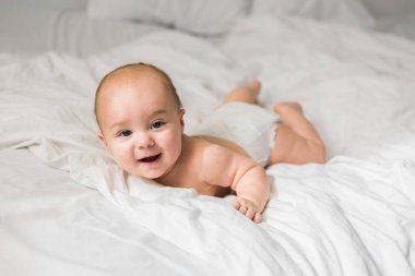 Evdeki beyaz yatakta gülümseyen yeni doğmuş bebek, sağlıklı bebek konsepti. Alfa ve alfa jenerasyonu..
