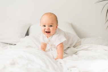 Evdeki beyaz yatakta gülümseyen yeni doğmuş bebek, sağlıklı bebek konsepti. Alfa ve alfa jenerasyonu..